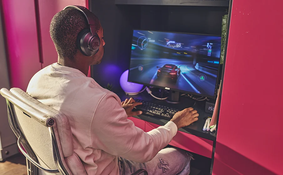 Cinco headsets gamer para PC, PS5 e Xbox: como escolher o ideal para você Pessoa usa o headset JBL Quantum 100M2 preto diante de um jogo de corrida no computador.